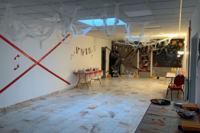 Salle décorée avec des tables rondes, nappes blanches et chaises rouges, prête pour un événement festif.