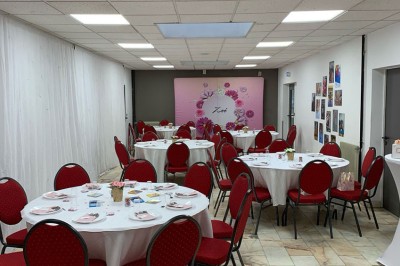 Salle décorée avec des tables rondes, nappes blanches et chaises rouges, prête pour un événement festif.