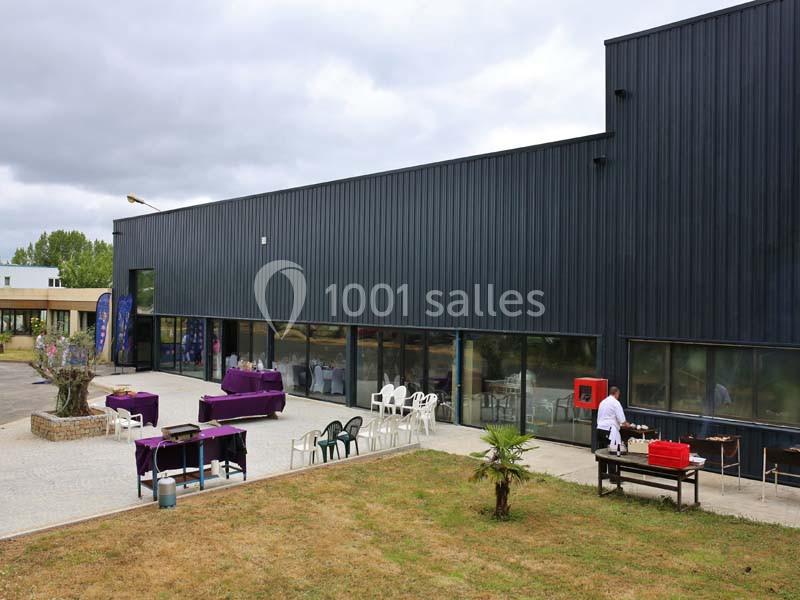 Façade d'un bâtiment moderne avec une terrasse aménagée, des tables dressées et un barbecue en extérieur.