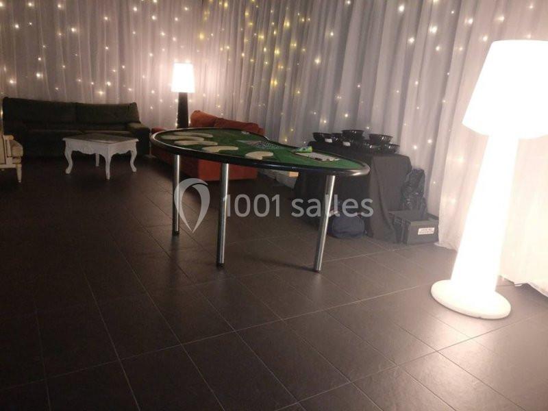 Table de jeu de casino dans une salle éclairée par des guirlandes lumineuses et des lampes, avec des canapés en arrière-plan.