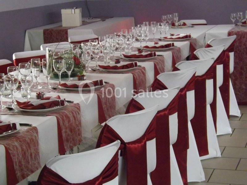 Tables de réception décorées avec nappes blanches, chemins de table rouges, chaises ornées de nœuds rouges et vaisselle…