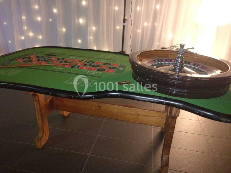 Table de roulette avec tapis de jeu vert et roue en bois, éclairée par des lumières en arrière-plan.