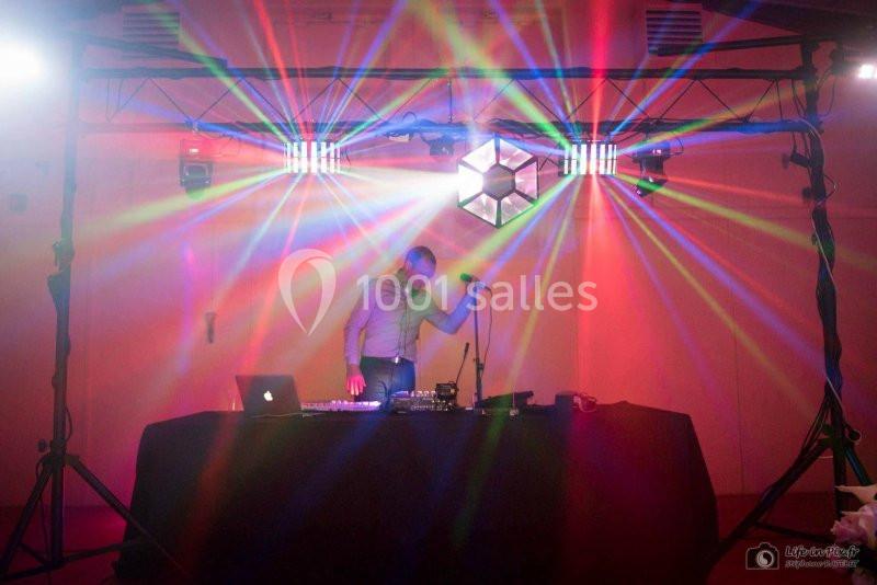 Un DJ mixe sur une table équipée d'un ordinateur, entouré de lumières colorées projetant des faisceaux.