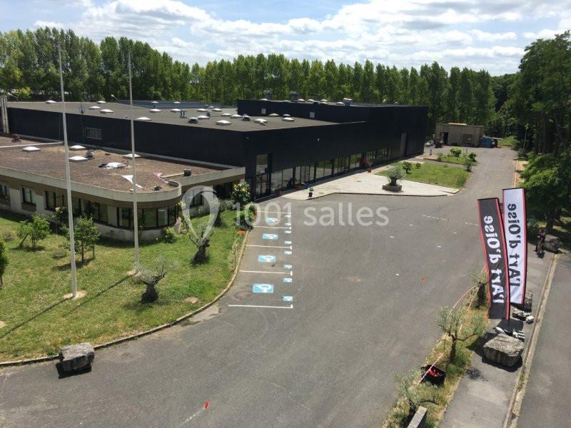 Vue aérienne d'un bâtiment moderne entouré d'espaces verts avec un parking comprenant des places pour personnes handicapées.
