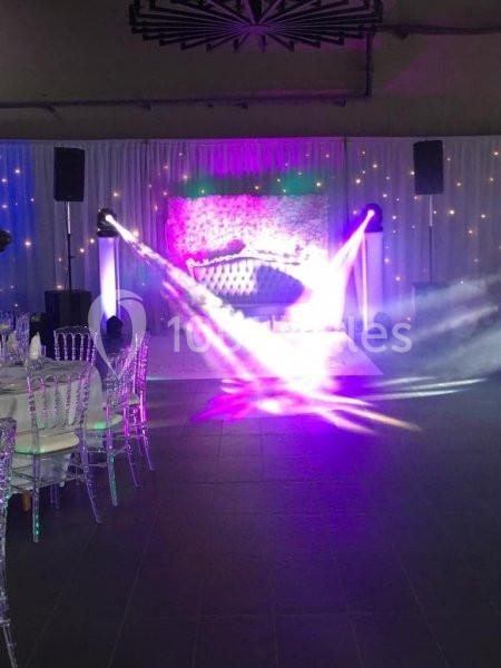 Salle de réception décorée avec des rideaux blancs, des chaises transparentes et des éclairages colorés projetés sur une…