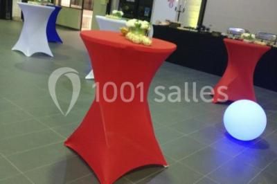 Salle de réception moderne avec tables hautes colorées, buffet en arrière-plan et éclairage suspendu.