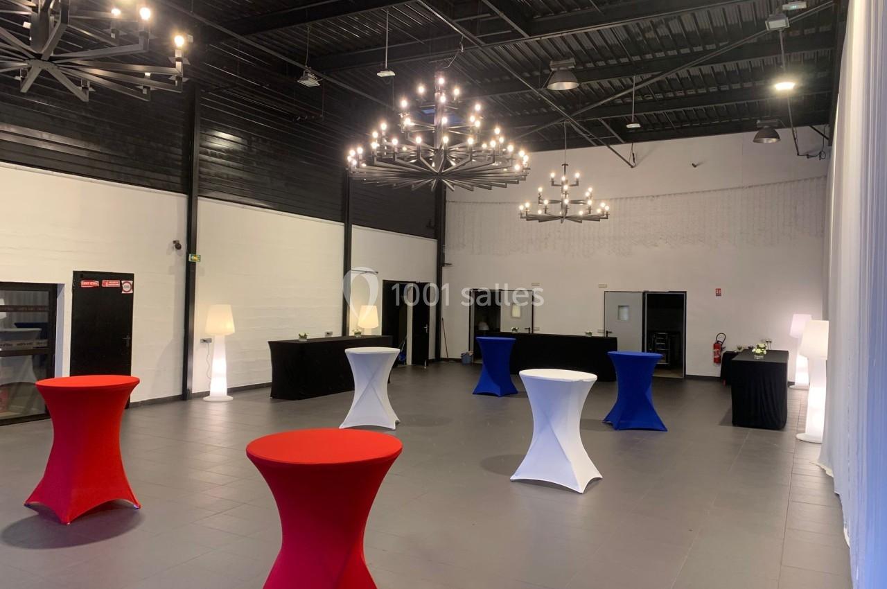 Salle de réception moderne avec tables hautes colorées, lustres suspendus et murs blancs et noirs.
