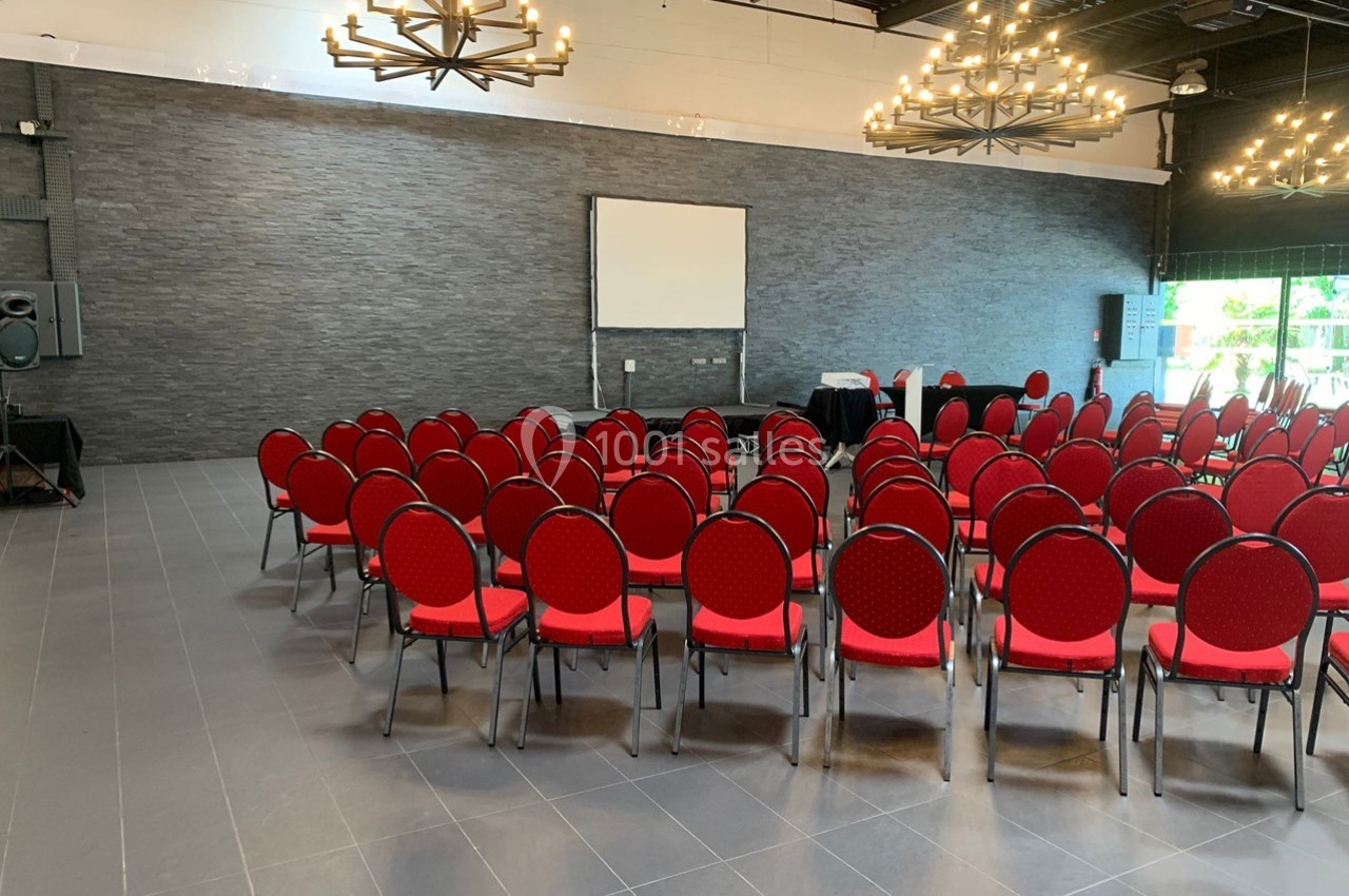 Salle de conférence avec des chaises rouges disposées en arc de cercle face à un écran de projection blanc.
