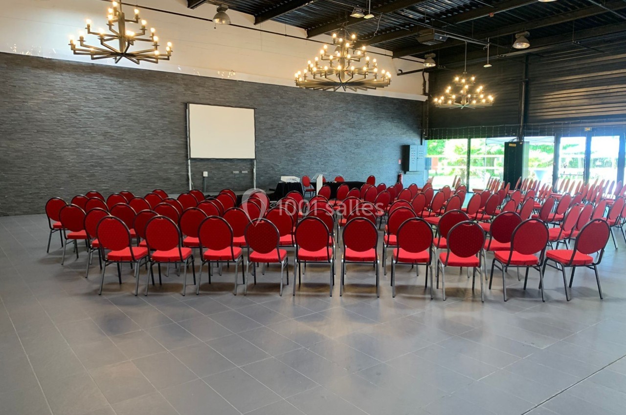 Salle de conférence avec des chaises rouges disposées en cercle autour d'un écran de projection.