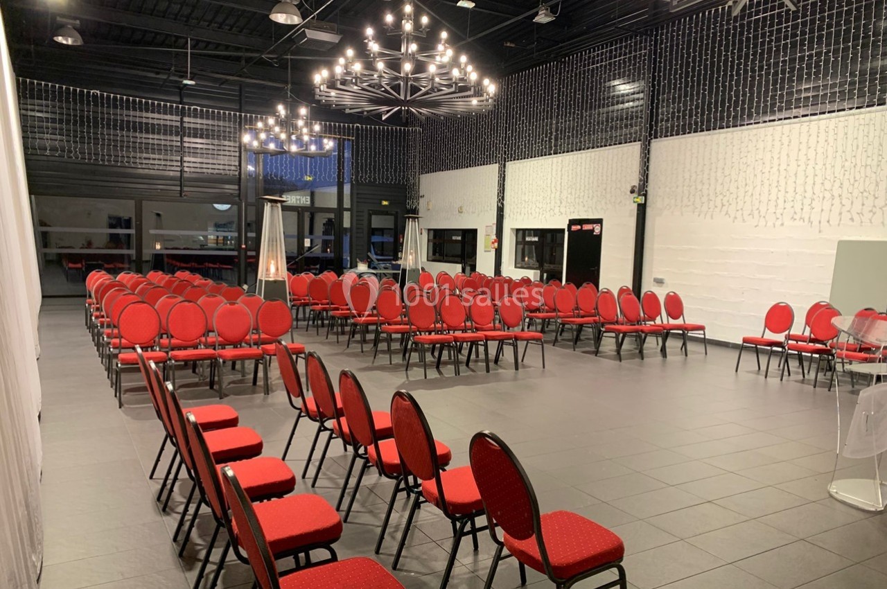 Salle de réception avec chaises rouges alignées, éclairée par des lustres modernes et des guirlandes lumineuses.