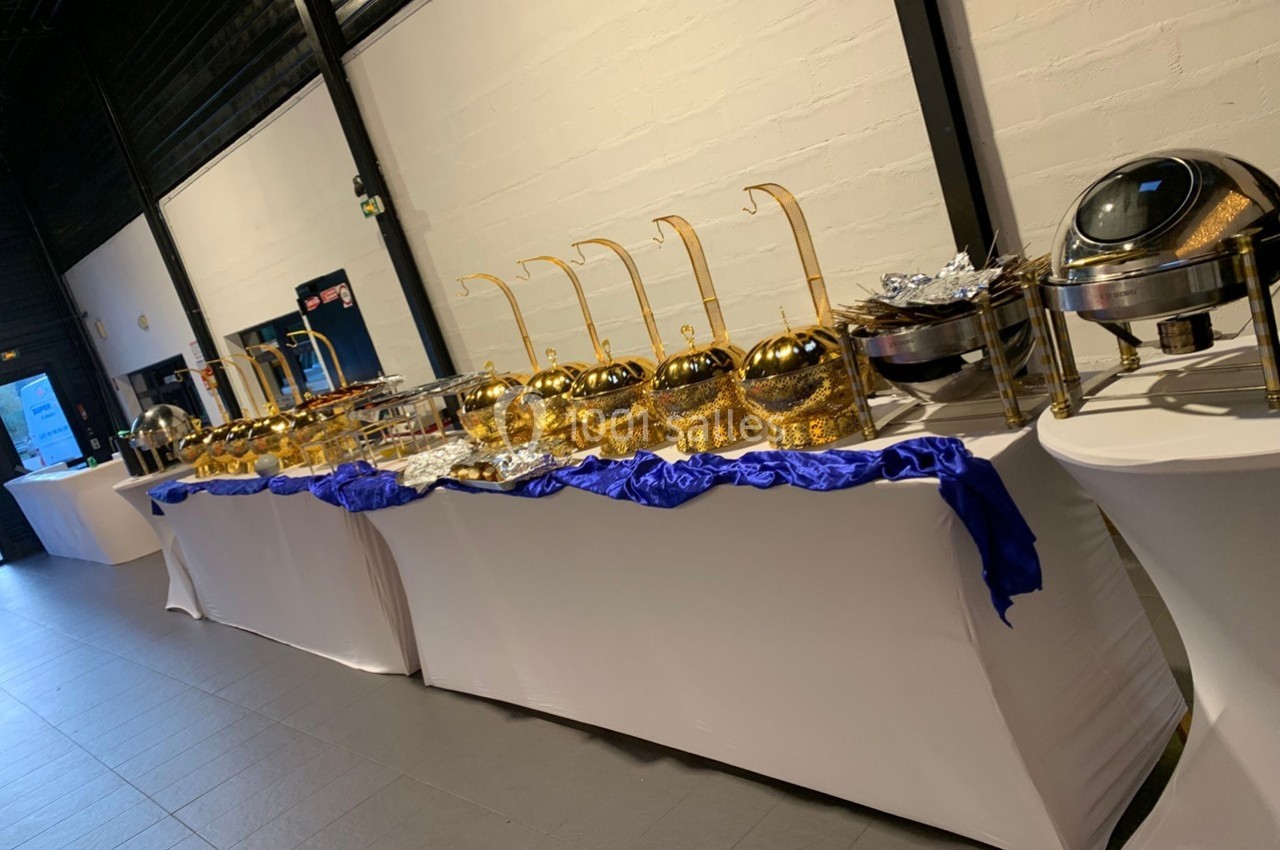 Buffet avec plats chauds présentés dans des récipients dorés et argentés sur des tables drapées de nappes blanches.