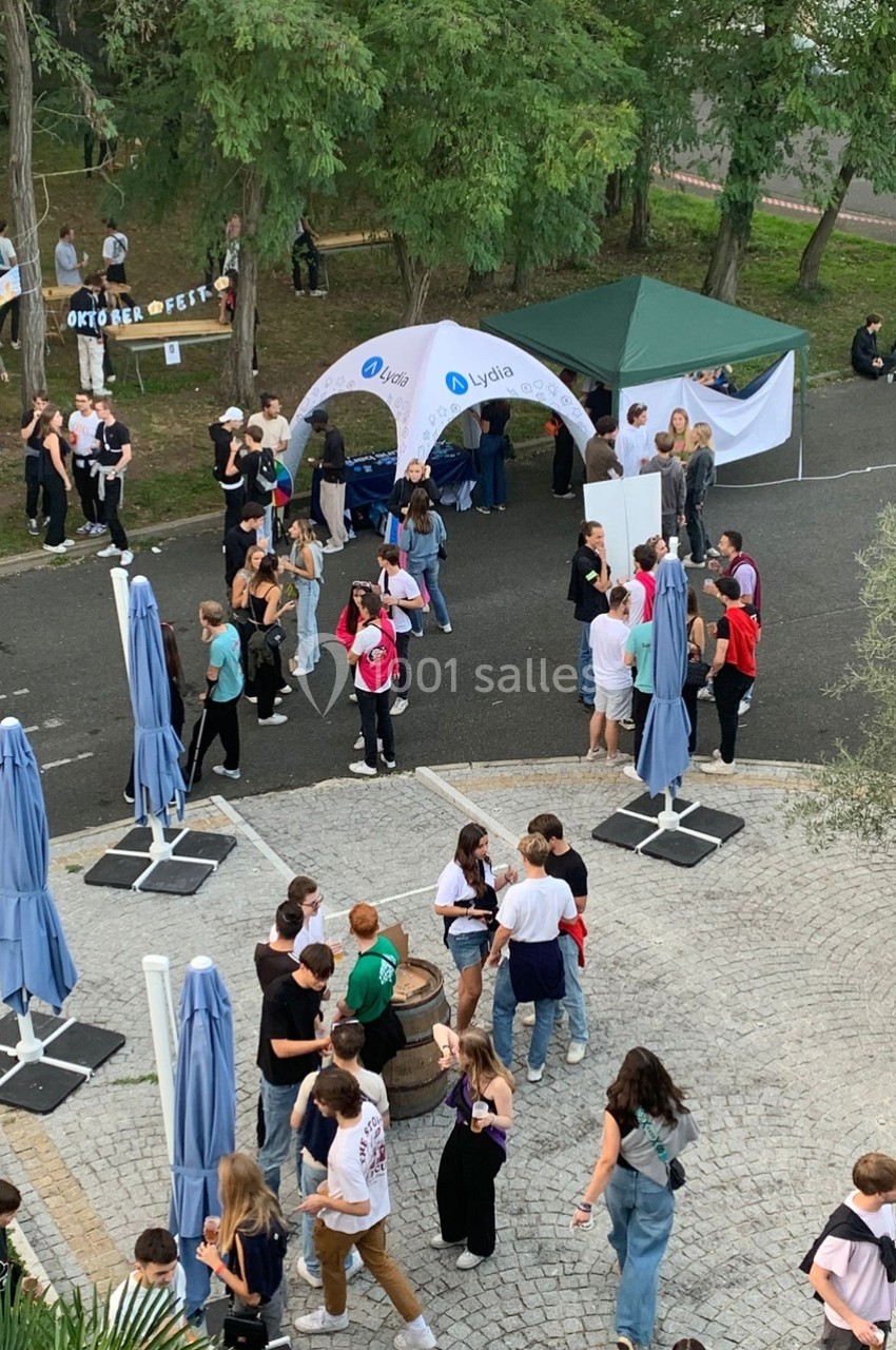 Groupe de personnes rassemblées en extérieur lors d'un événement avec stands et décorations sous des arbres.