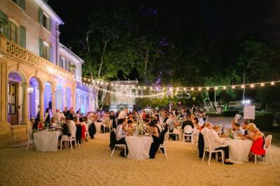 Vue aérienne d'une grande maison de style provençal avec des tables dressées pour un événement en extérieur.