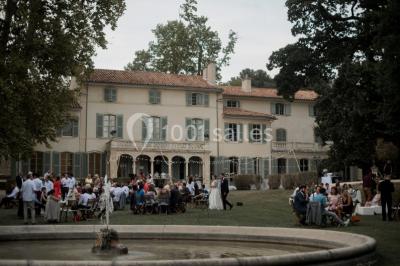 Vue aérienne d'une grande maison de style provençal avec des tables dressées pour un événement en extérieur.
