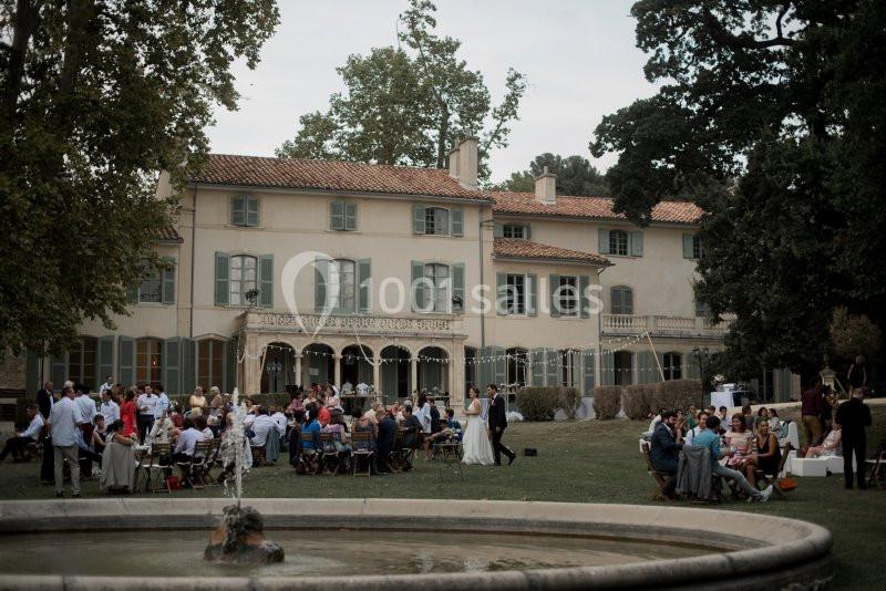 Groupe de personnes rassemblées dans un jardin devant une grande maison ancienne, avec une fontaine au premier plan.