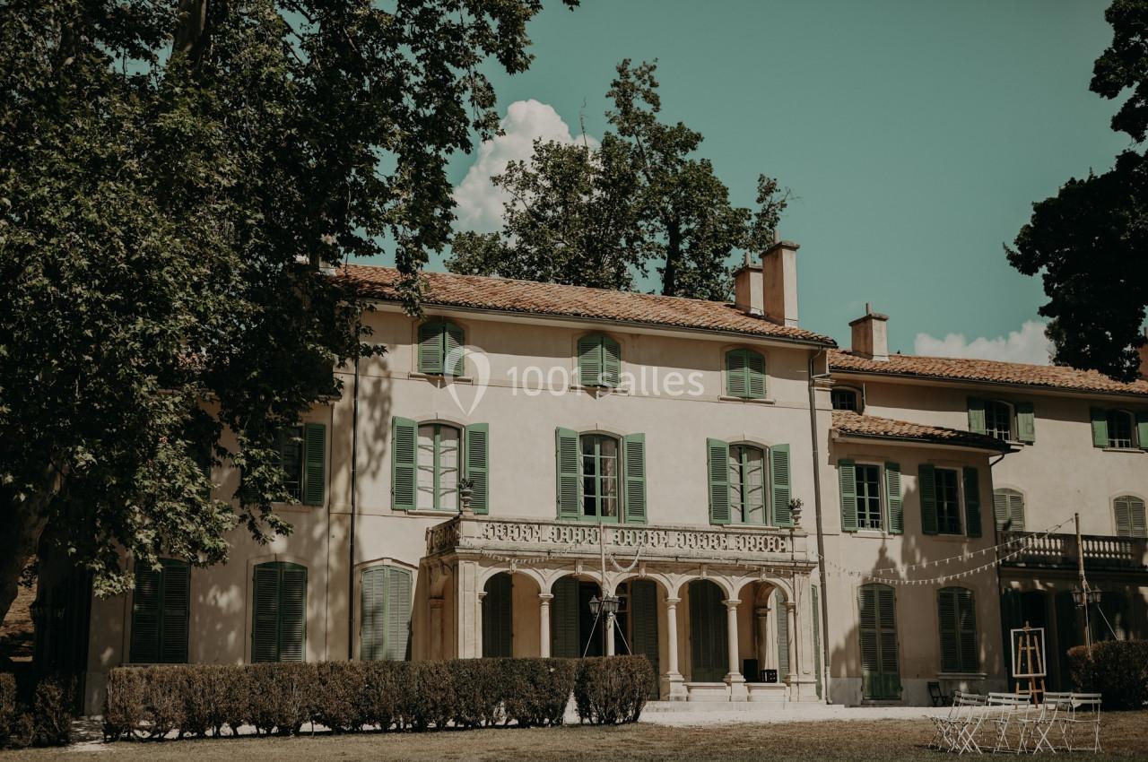 Façade d'une grande maison ancienne avec volets verts, entourée d'arbres et d'une pelouse.