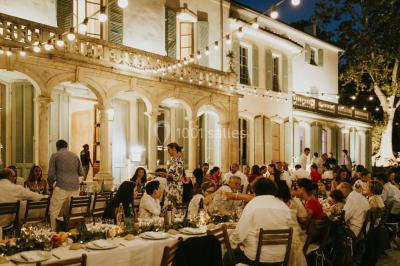 Vue aérienne d'une grande maison de style provençal avec des tables dressées pour un événement en extérieur.