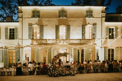 Vue aérienne d'une grande maison de style provençal avec des tables dressées pour un événement en extérieur.