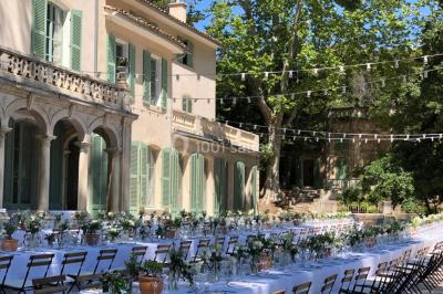 Vue aérienne d'une grande maison de style provençal avec des tables dressées pour un événement en extérieur.
