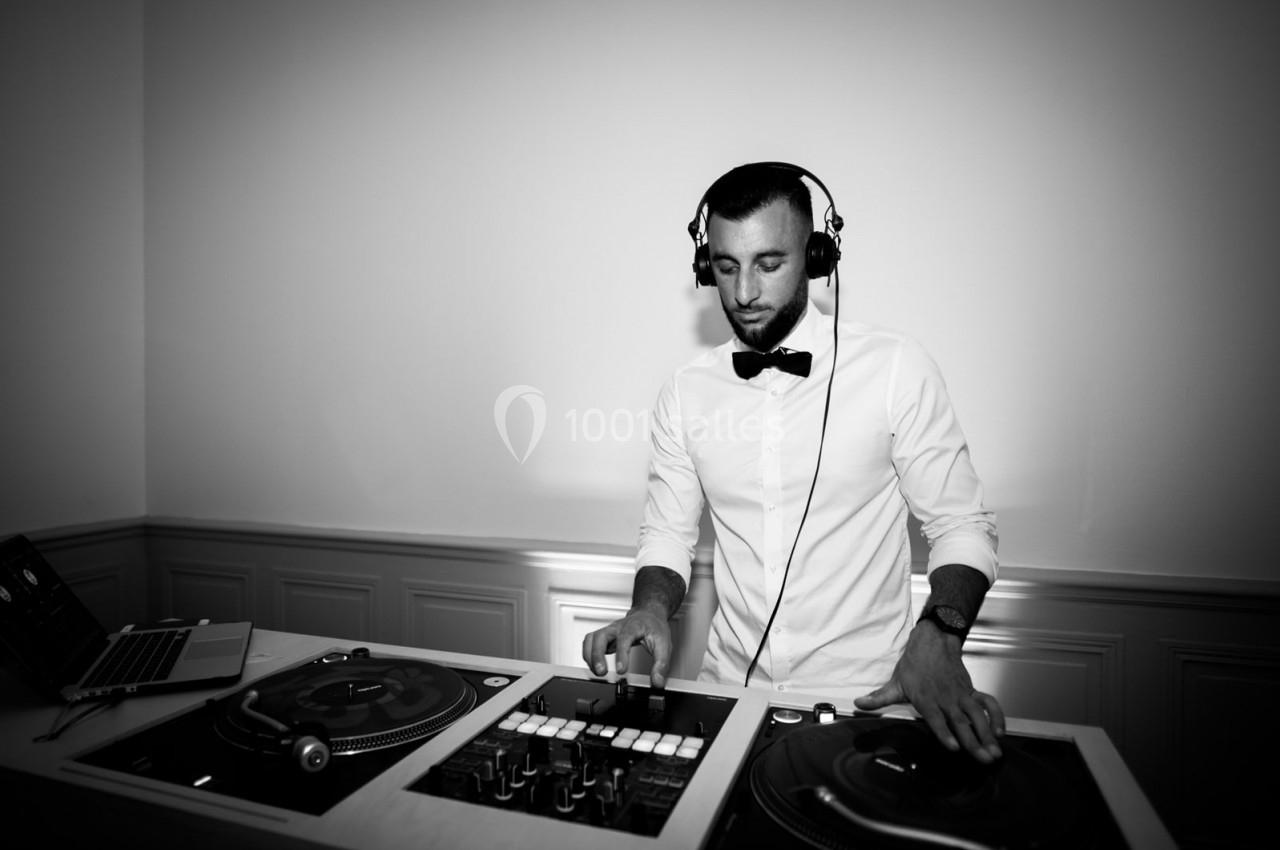 Un DJ en chemise blanche et nœud papillon mixe sur des platines dans une ambiance sobre et élégante.