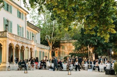 Vue aérienne d'une grande maison de style provençal avec des tables dressées pour un événement en extérieur.