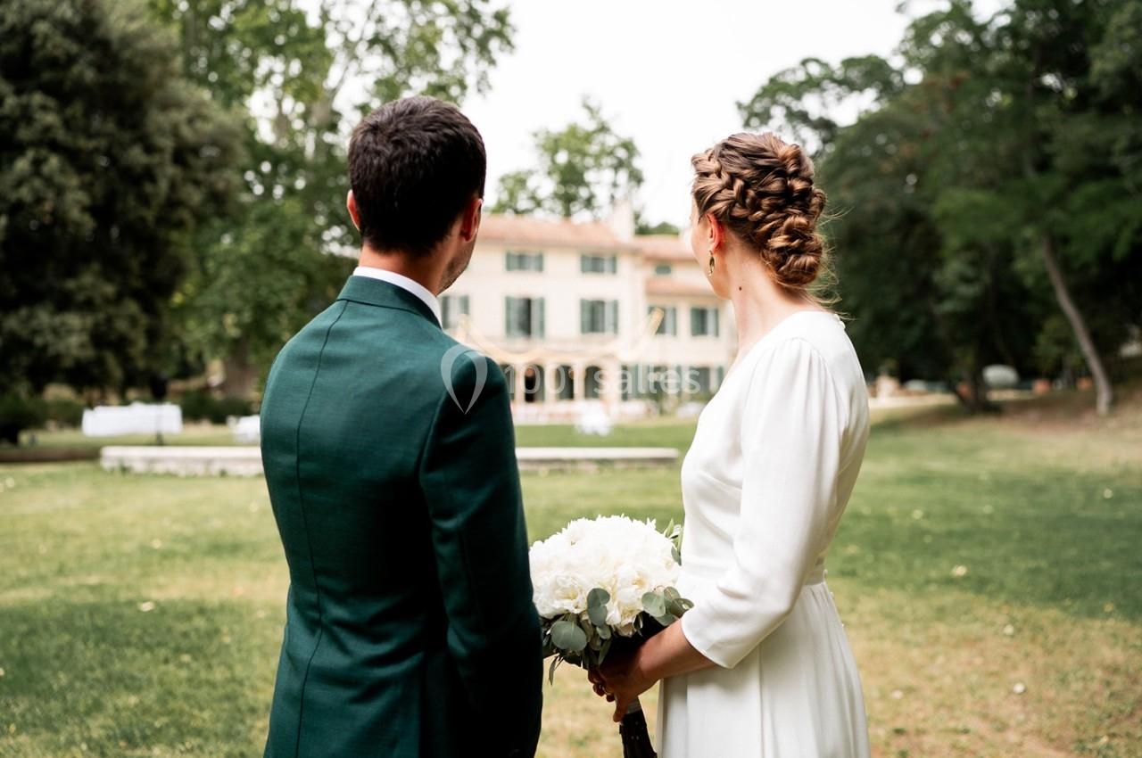 Un couple de dos, vêtu élégamment, regarde une grande maison entourée de verdure.