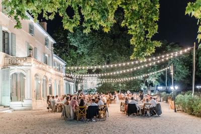 Vue aérienne d'une grande maison de style provençal avec des tables dressées pour un événement en extérieur.