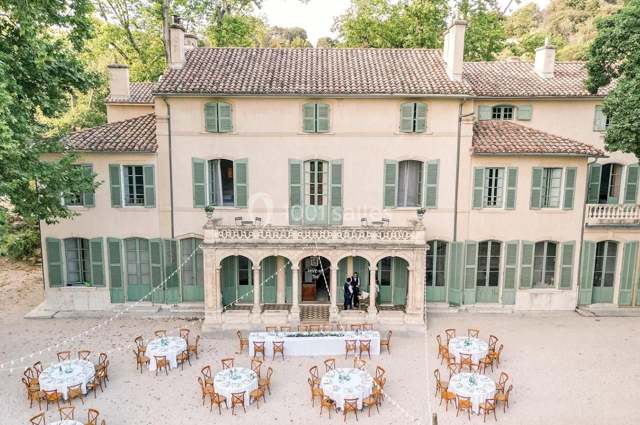 Vue aérienne d'une grande maison de style provençal avec des tables dressées pour un événement en extérieur.