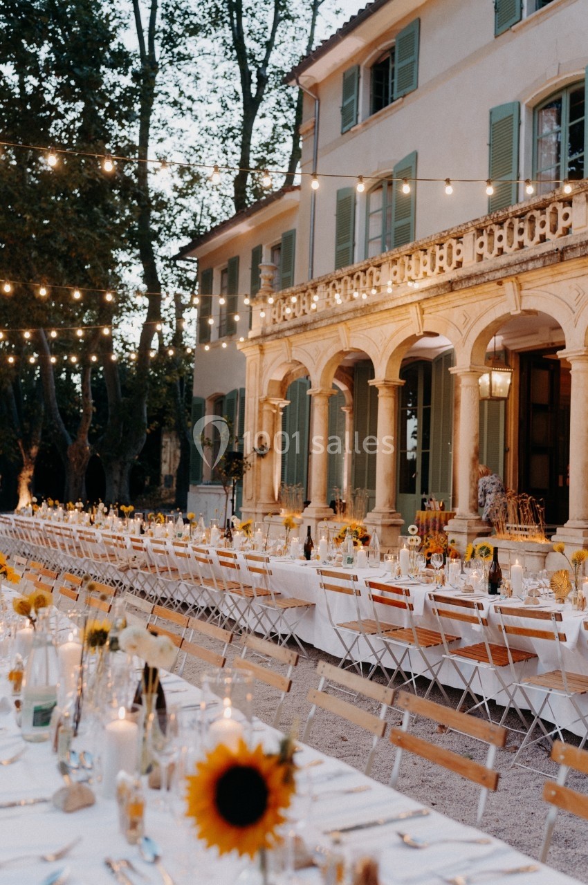 Location salle Marseille 14 (Bouches-du-Rhône) - Bastide de Toursainte #87 Grande table dressée en extérieur avec des guirlandes lumineuses, devant une maison élégante entourée d'arbres.