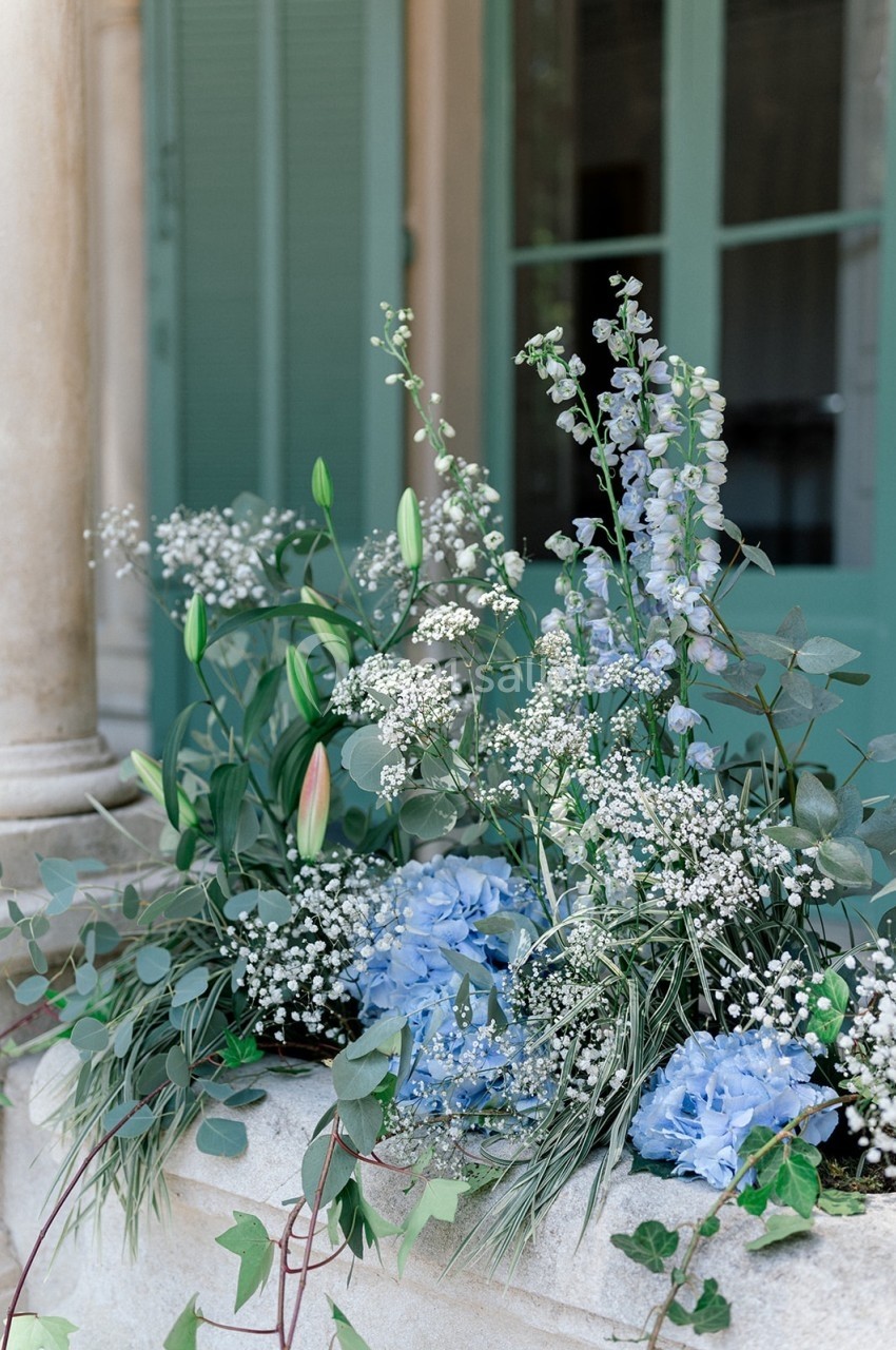 Location salle Marseille 14 (Bouches-du-Rhône) - Bastide de Toursainte #90 Composition florale avec hortensias bleus, gypsophiles, lys et feuillage, disposée devant une fenêtre à volets verts.