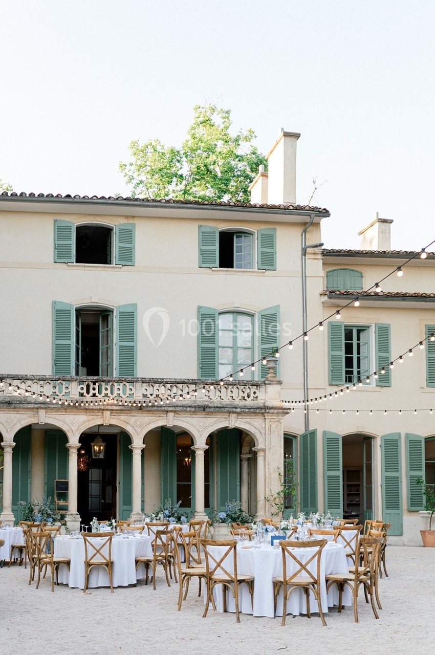Location salle Marseille 14 (Bouches-du-Rhône) - Bastide de Toursainte #92 Tables dressées pour un repas en plein air devant une grande maison aux volets verts, éclairée par des guirlandes lumineuses.