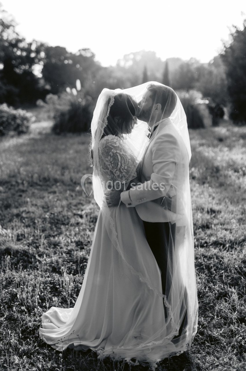 Location salle Marseille 14 (Bouches-du-Rhône) - Bastide de Toursainte #94 Un couple en tenue de mariage s'embrasse tendrement dans un champ, enveloppé d'un voile.