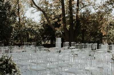 Miniature Location salle Marseille 14 (Bouches-du-Rhône) - Bastide de Toursainte #99 Chaises transparentes disposées en rangées sur une allée blanche, entourées d'arbres dans un cadre extérieur.