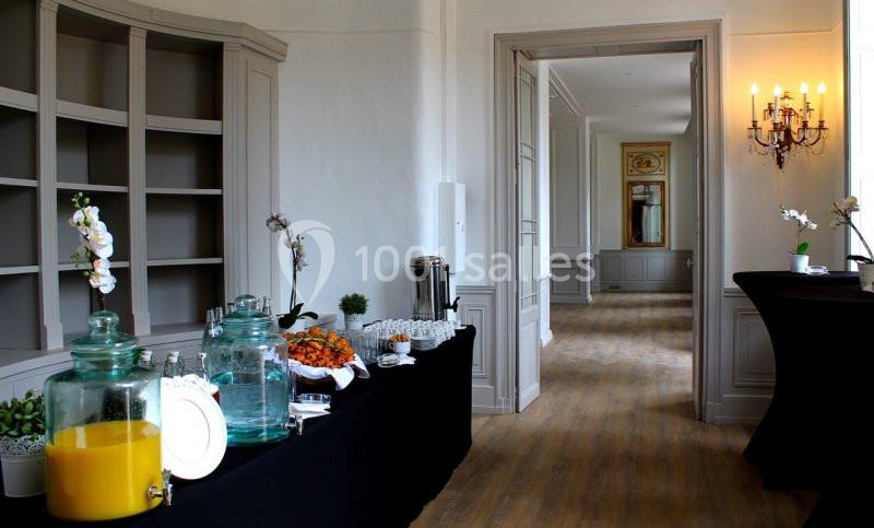 Table de buffet avec boissons, fruits et viennoiseries dans une salle lumineuse au décor élégant et épuré.
