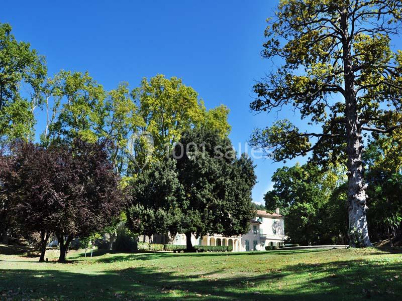 Grande maison entourée d'arbres dans un parc verdoyant sous un ciel bleu dégagé.