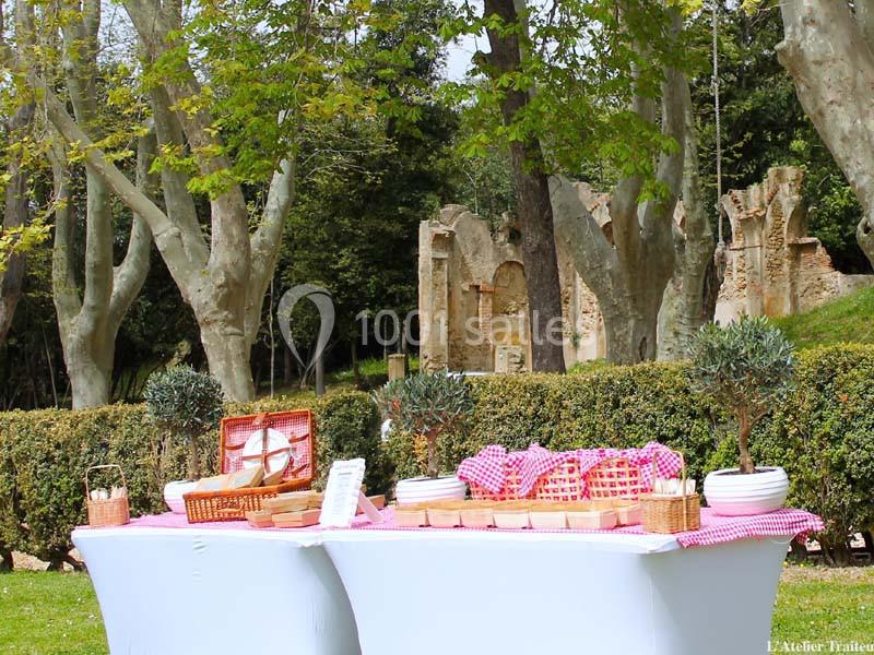 Table de buffet en plein air avec nappes blanches, paniers en osier et plats disposés dans un parc arboré.