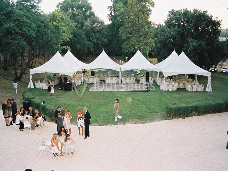 Tentes blanches installées sur une pelouse pour un événement, avec des tables dressées et des invités discutant à l…