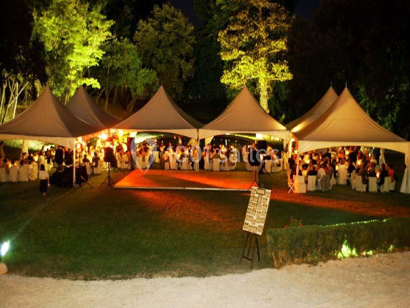 Tentes blanches éclairées abritant des tables et des invités lors d'un événement en plein air, de nuit.