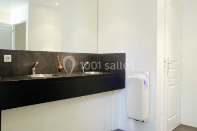 Deux lavabos avec miroir mural, sèche-mains mural blanc et décoration minimaliste dans une salle de bain moderne.