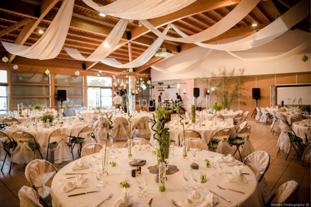 Salle de réception décorée avec des tables rondes, nappes blanches, centres de table fleuris et drapés suspendus.