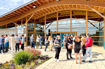 Vue d'une prairie verdoyante avec un grand arbre à gauche et des bâtiments ruraux sous un ciel dégagé.