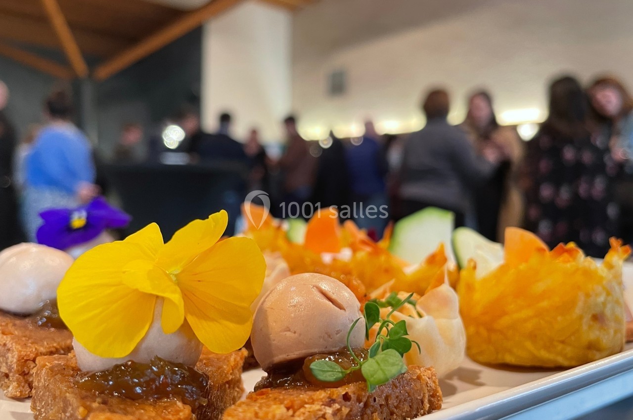 Plateau de bouchées colorées et raffinées avec des fleurs comestibles, en arrière-plan un groupe de personnes flou.
