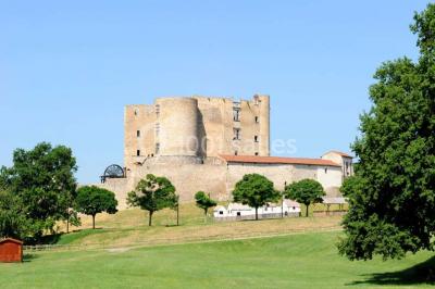 Vue d'une prairie verdoyante avec un grand arbre à gauche et des bâtiments ruraux sous un ciel dégagé.