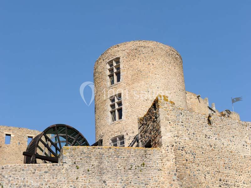 Tour en pierre d'un château médiéval avec une roue en bois, sous un ciel bleu dégagé.