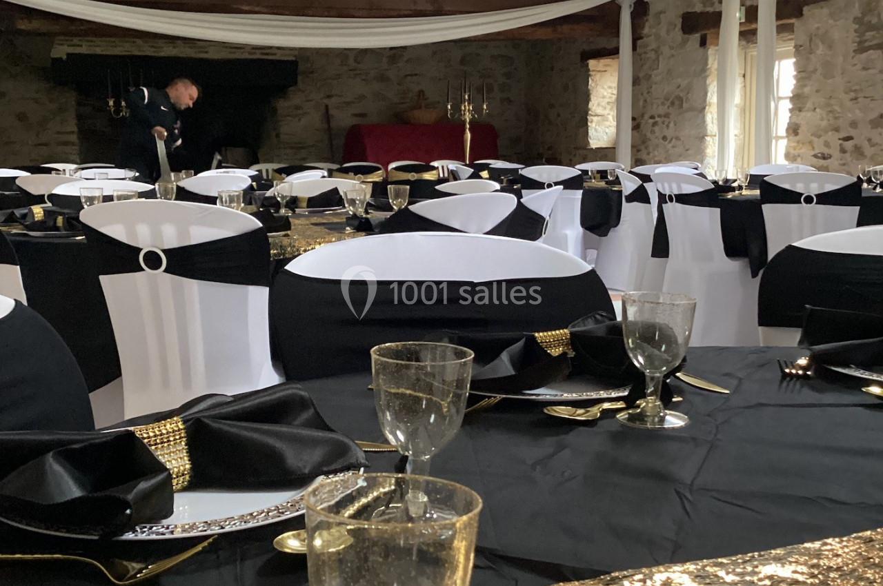 Salle de réception décorée avec des tables dressées en noir, blanc et or, sous un plafond avec drapés blancs.