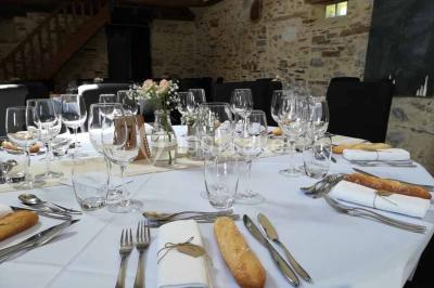 Salle à manger rustique avec table en bois dressée, mur en pierre apparente, étagères intégrées et cuisine ouverte.