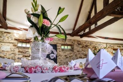 Salle à manger rustique avec table en bois dressée, mur en pierre apparente, étagères intégrées et cuisine ouverte.