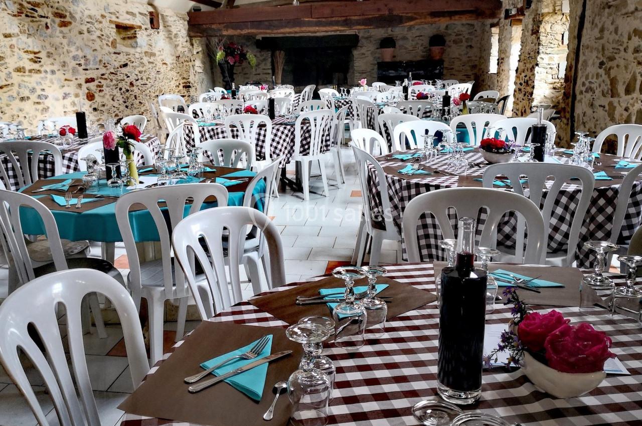 Salle rustique décorée pour un repas, avec tables dressées, nappes à carreaux et chaises blanches en plastique.