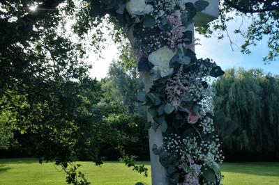 Salle à manger rustique avec table en bois dressée, mur en pierre apparente, étagères intégrées et cuisine ouverte.
