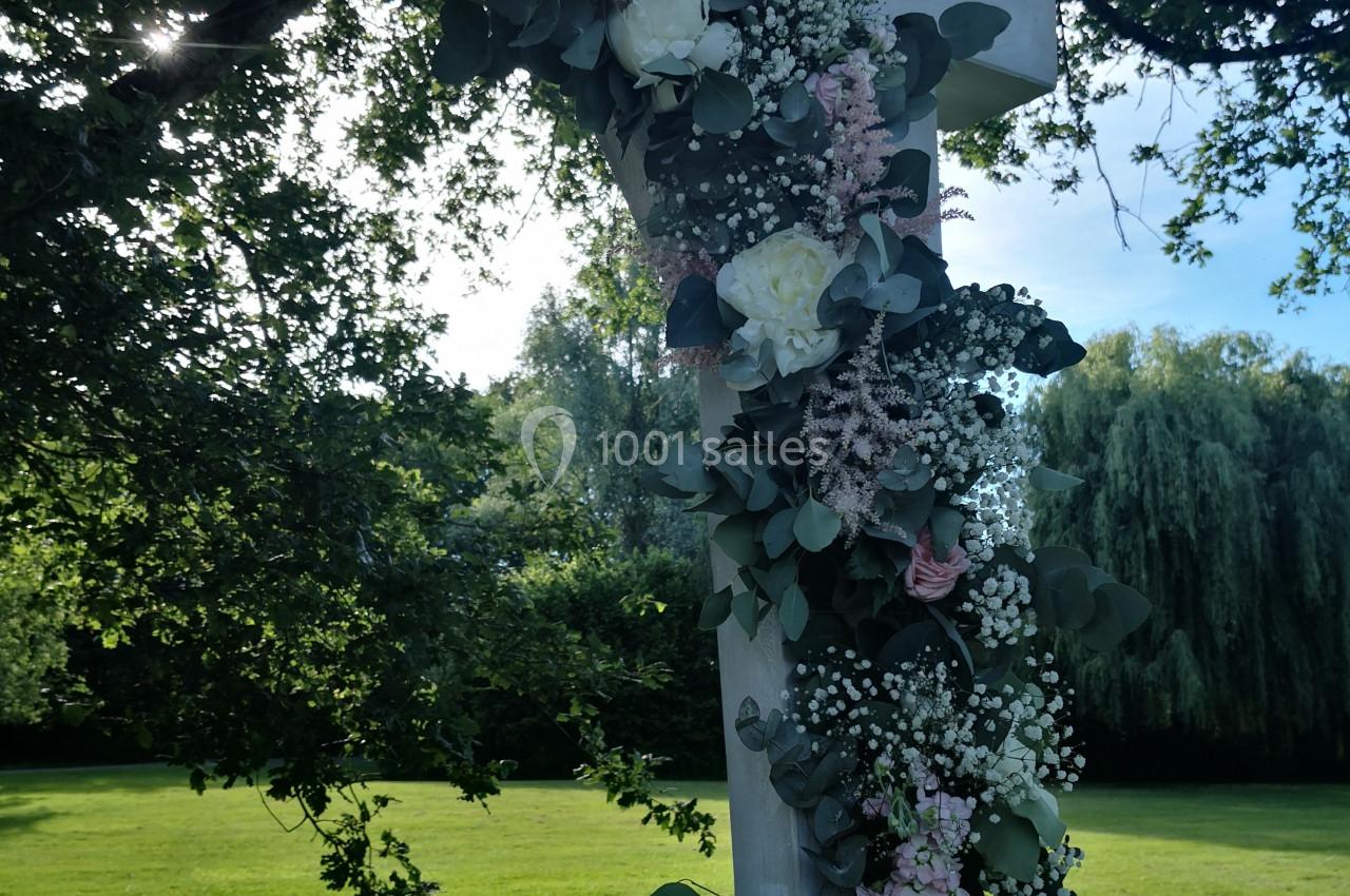 Arche en bois décorée de fleurs blanches et roses avec feuillage, installée dans un jardin verdoyant.